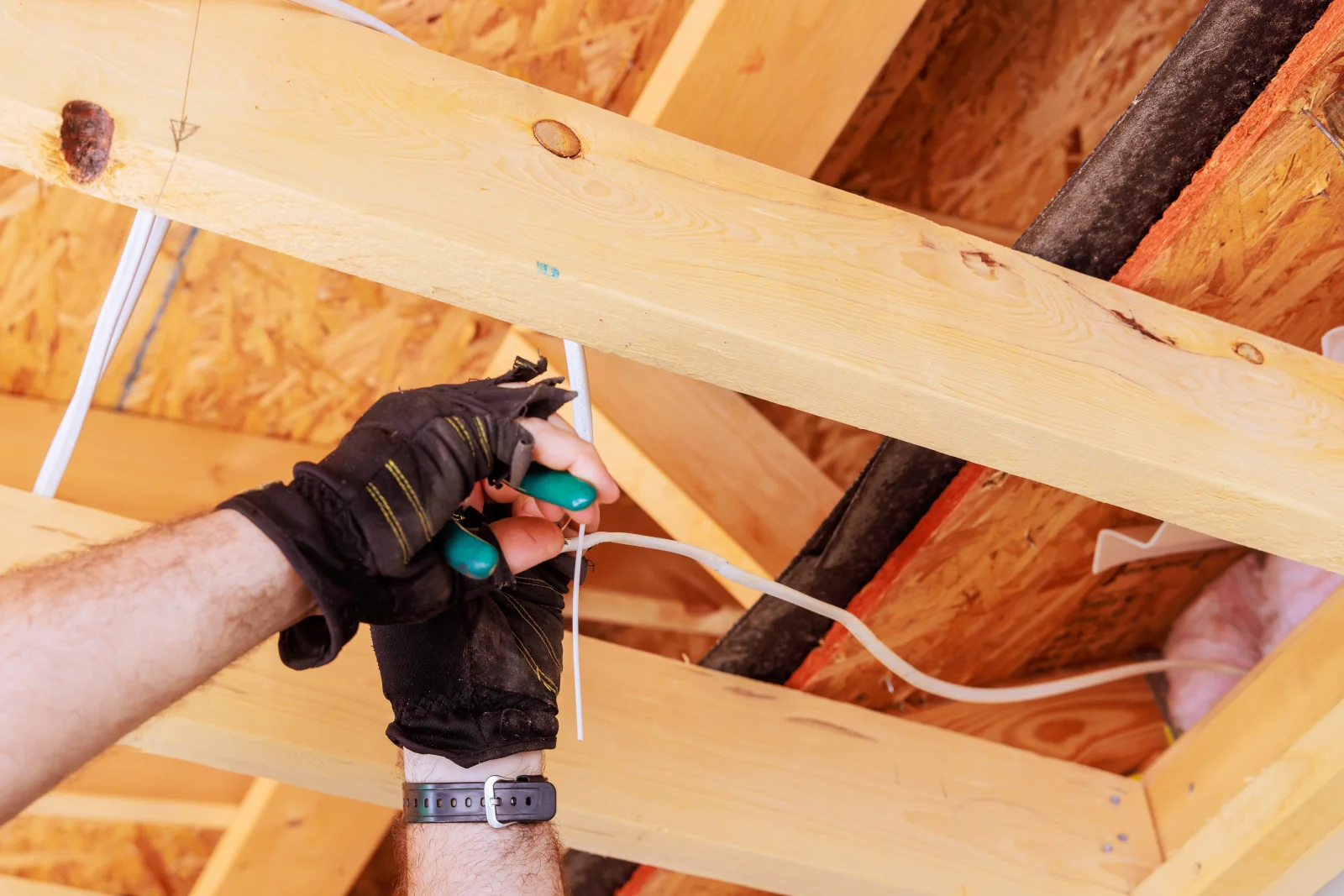 An electrician running low-voltage wiring through attic joists for an interconnected smoke detector system in a Phoenix home.