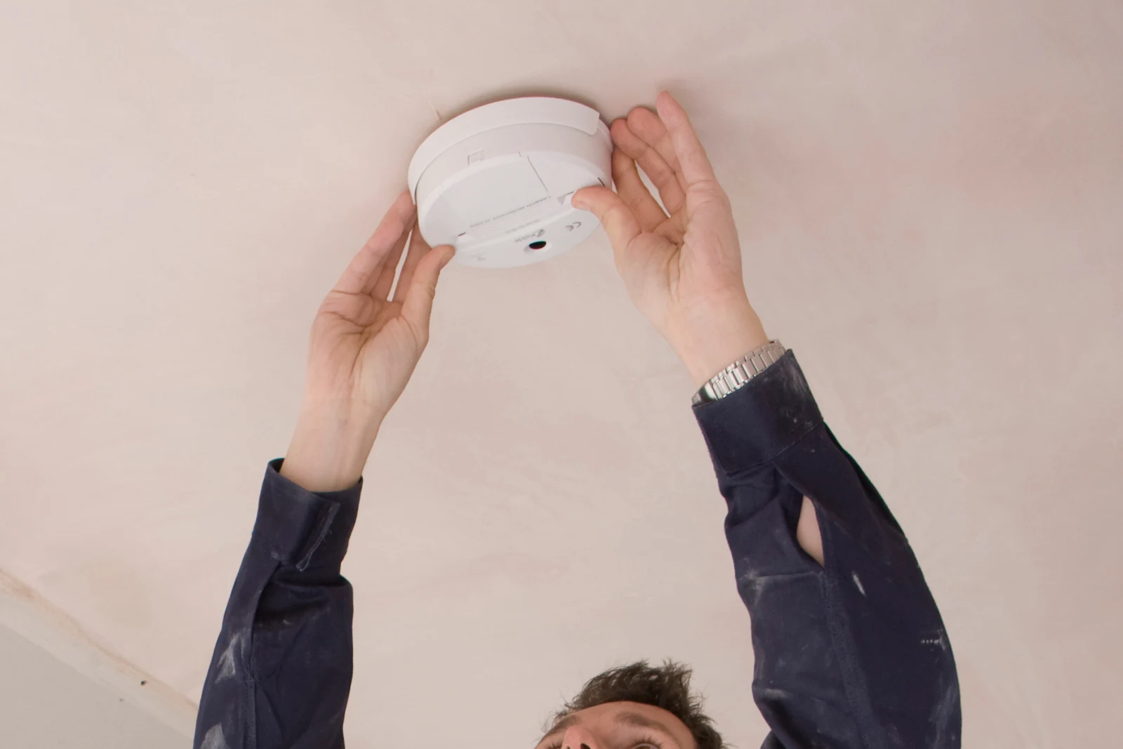 smoke-detector-repair-phoenix-installation An electrician installing a new smoke detector on the ceiling of a Phoenix home during a repair visit.