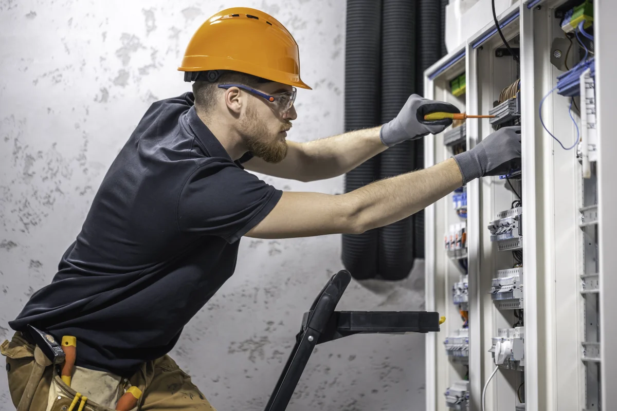 surge-protector-installation-phoenix-electrical-panel-technician Surge protector installation in Phoenix, Arizona — an electrician in a hard hat, safety glasses, and gloves working on a residential electrical panel.
