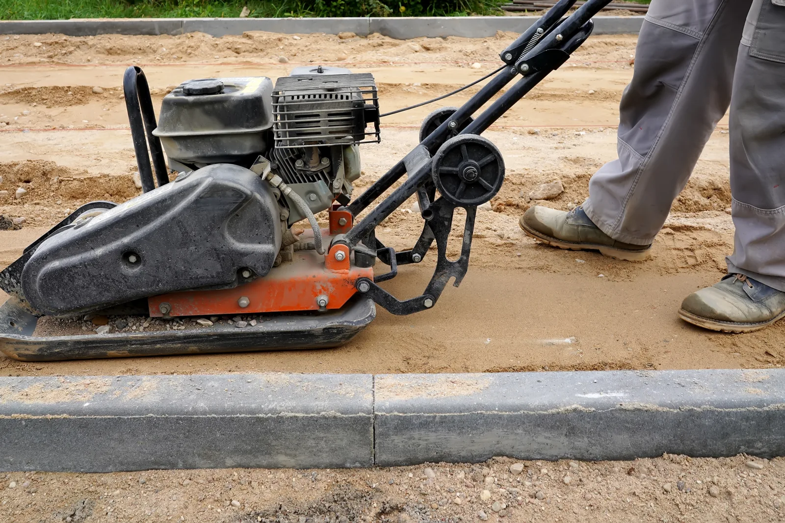 synthetic-grass-phoenix-base-prep-compaction A crew compacting a crushed granite base for synthetic grass installation on Phoenix, Arizona's caliche soil before the turf is laid.