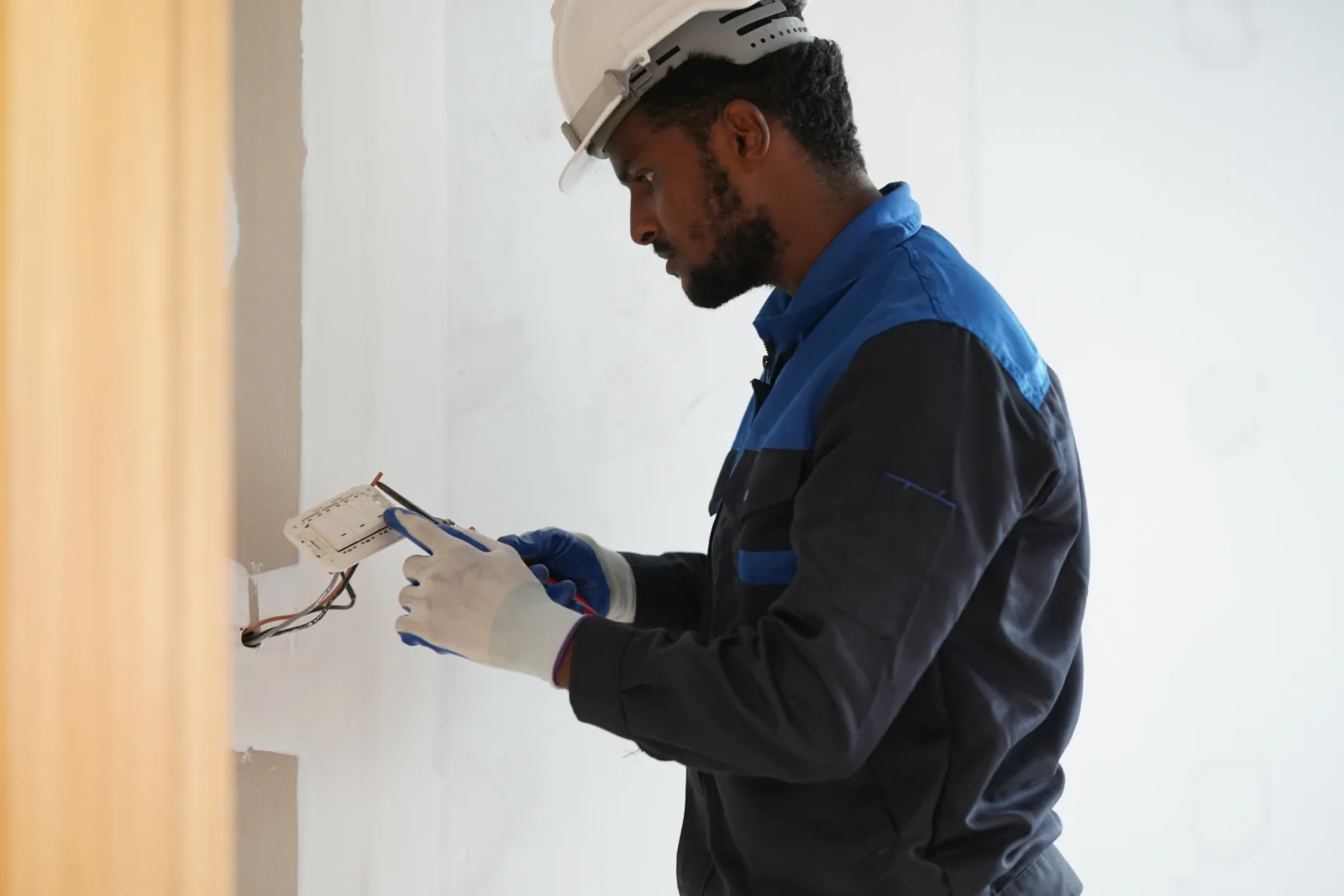 thermostat-repair-phoenix-wiring-check An HVAC technician checking low-voltage thermostat wiring behind a wall-mounted unit in a Phoenix home, the kind of heat-driven wiring failure common after a hot summer.
