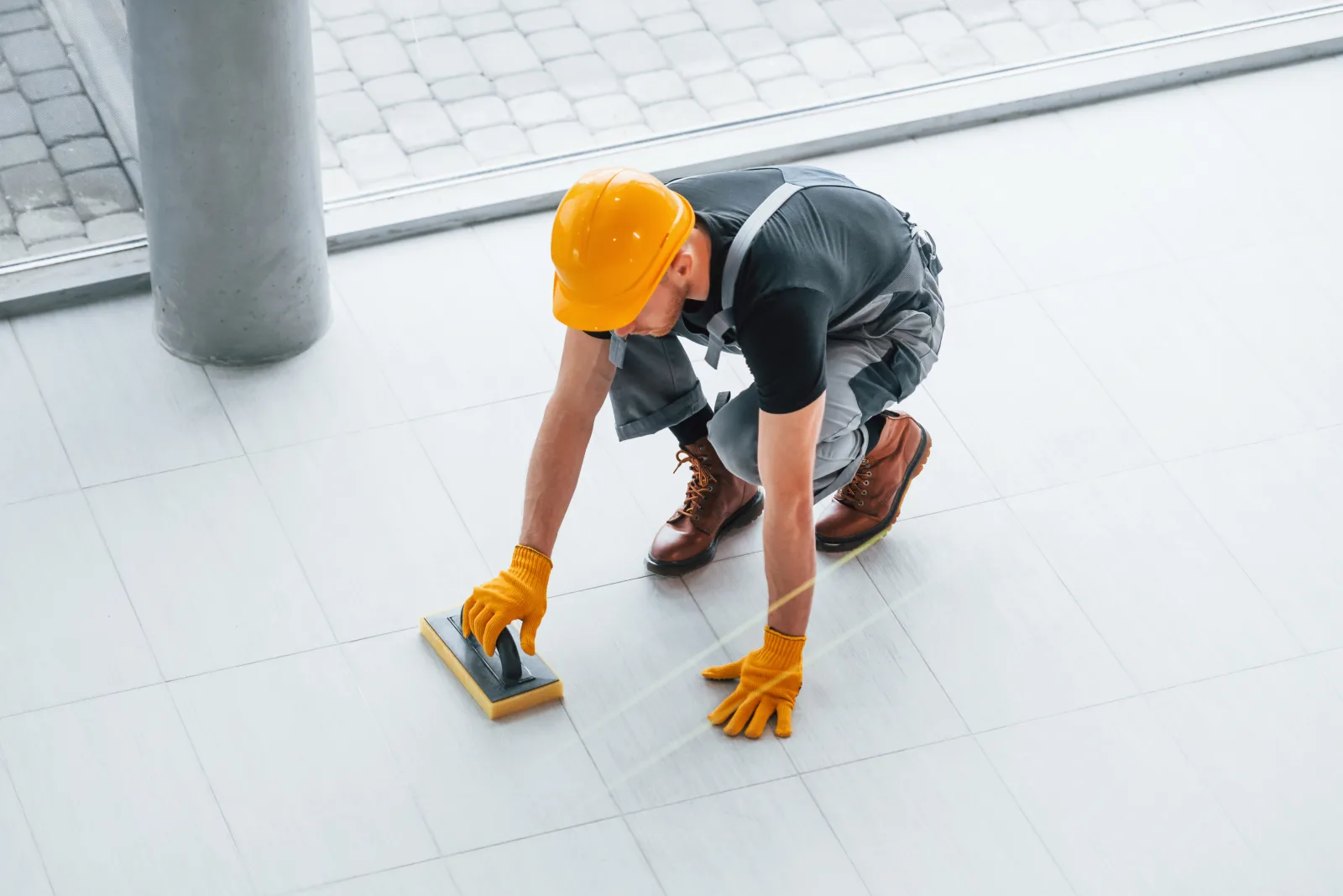 tile-and-grout-cleaning-phoenix-az-grout-line-hand-scrubbing Tile and grout cleaning in Phoenix, Arizona — a technician in a hard hat scrubbing tile grout lines by hand on a floor.