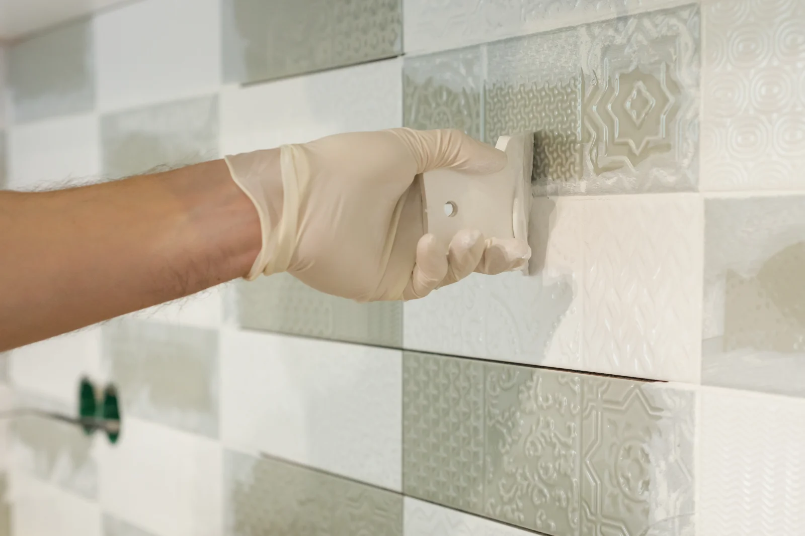 A tile repair pro pressing and grouting a replacement patterned wall tile to match the surrounding tile.
