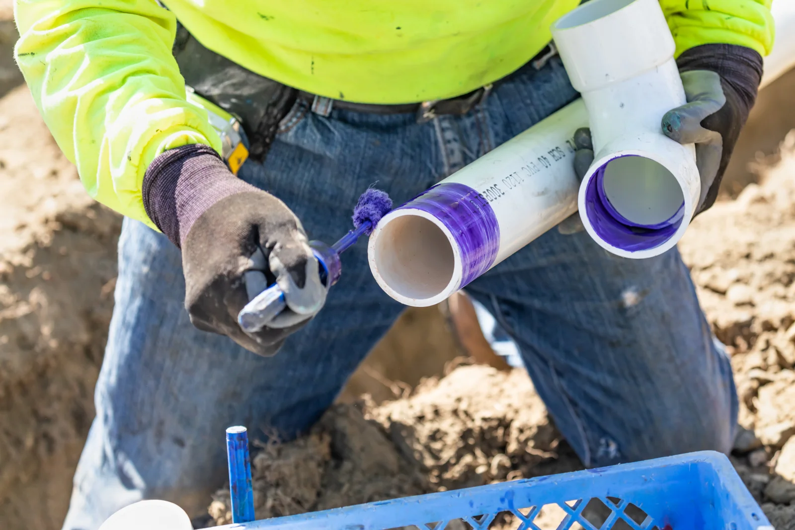 A plumber preparing a PVC pipe fitting for a trenchless sewer repair connection with primer and glue.
