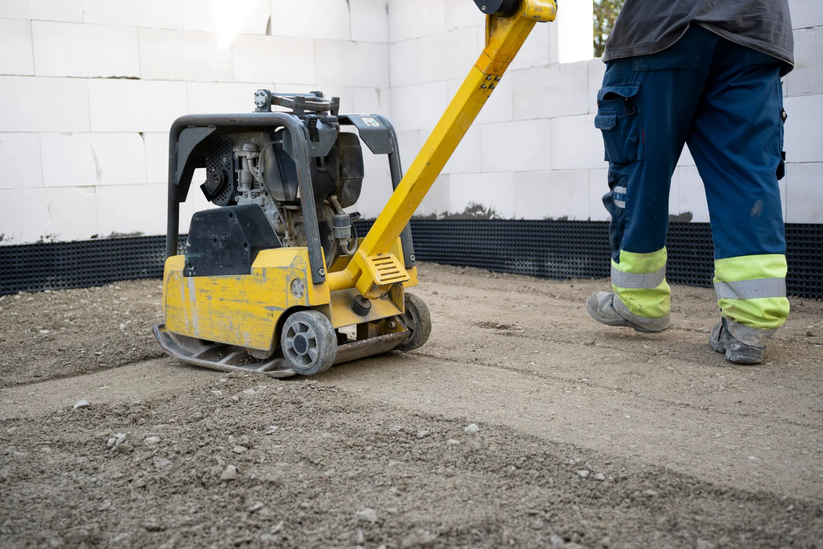 turf-installation-phoenix-base-compaction-plate-compactor A professional in hi-vis workwear operating a plate compactor to compact the gravel sub-base before a Phoenix turf installation.