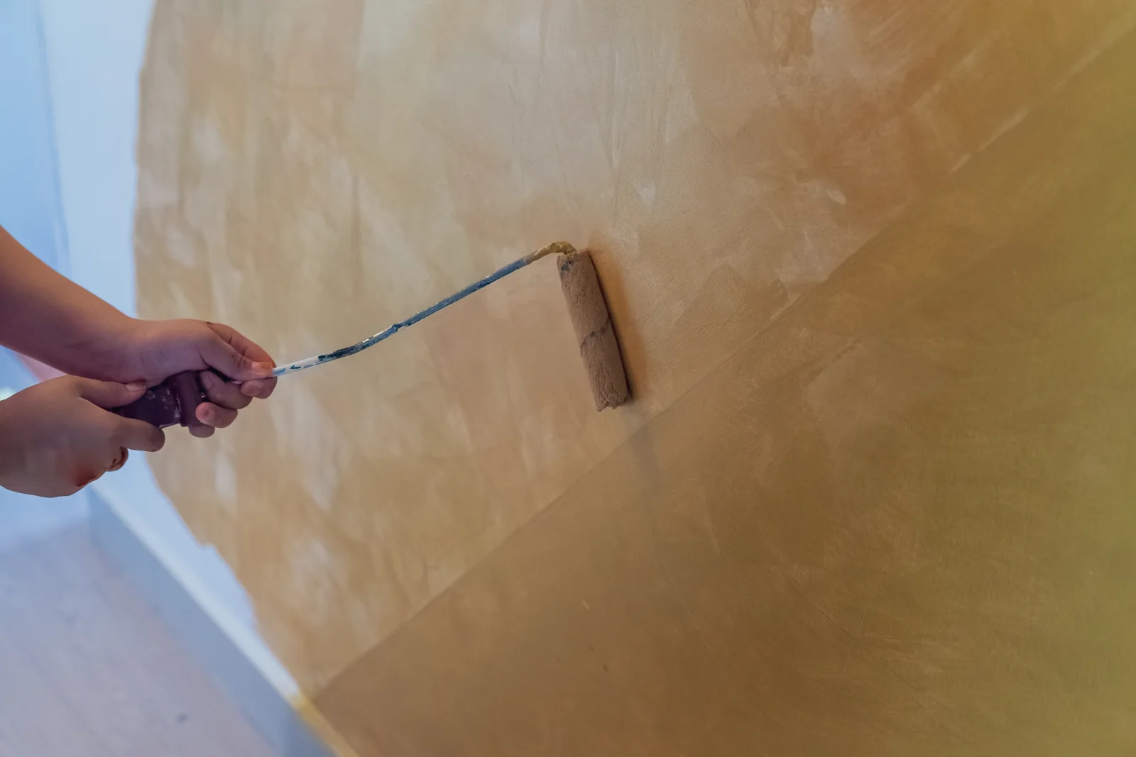 Close-up of hands applying Venetian plaster with a small steel trowel, building up a warm gold-toned polished layer in Phoenix, Arizona.