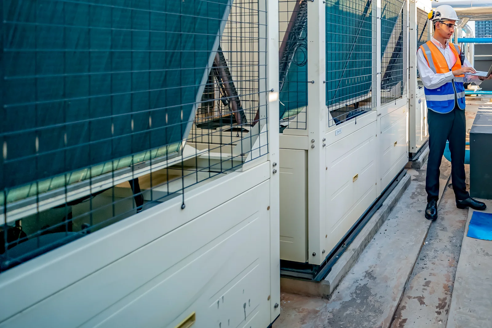 walk-in-cooler-repair-phoenix-condenser A commercial refrigeration technician in a hard hat and safety vest inspecting rooftop condenser units that serve walk-in coolers at a Phoenix business.