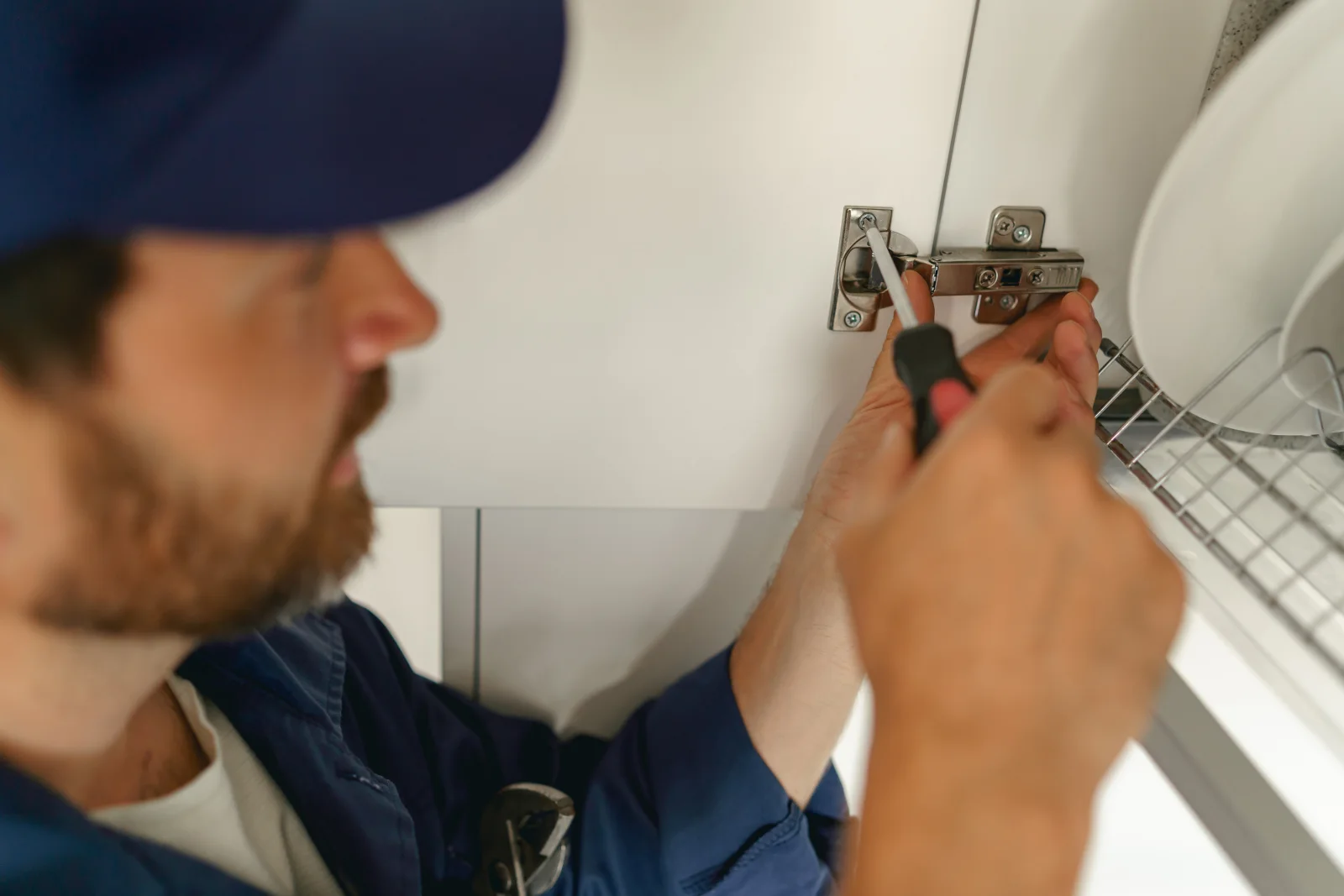 walk-in-cooler-repair-phoenix-inspection A commercial refrigeration technician adjusting a walk-in cooler door hinge with a screwdriver to fix a seal that was letting in warm air.