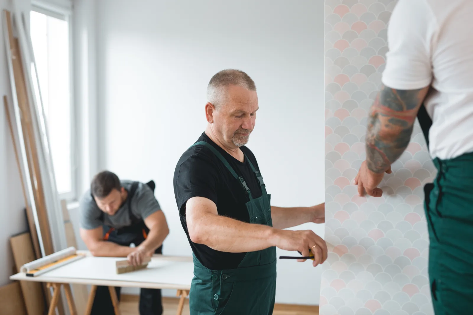 wallpaper-installation-phoenix-professional-crew Wallpaper installation in Phoenix, Arizona — a two-person professional crew measuring and aligning a wallpaper pattern before hanging it.