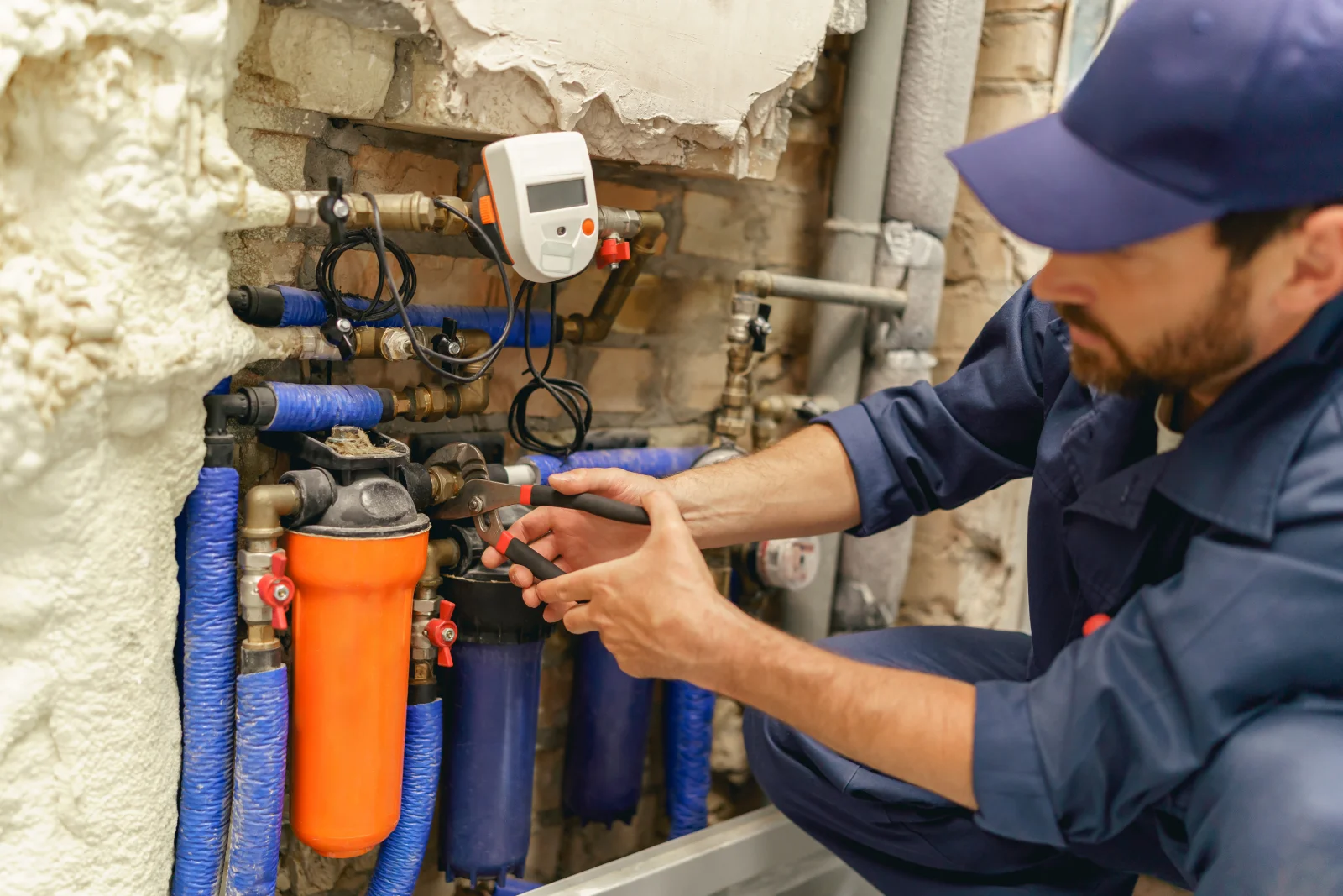 water-softener-installation-phoenix-plumbing-connections Water softener installation in Phoenix, Arizona — a technician connecting plumbing fittings on a whole-house water filtration system with blue-wrapped pipes.