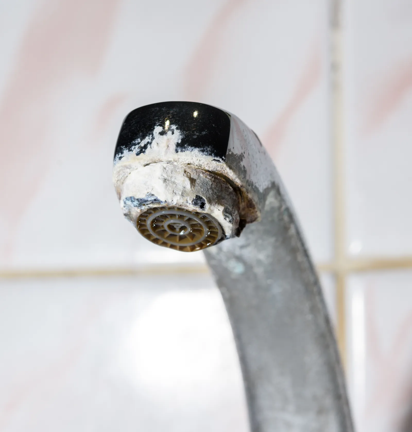 Heavy white hard-water limescale crusted on a Phoenix home faucet aerator, the mineral scale that a failed or undersized water softener lets build up on fixtures, water heaters, and appliances.