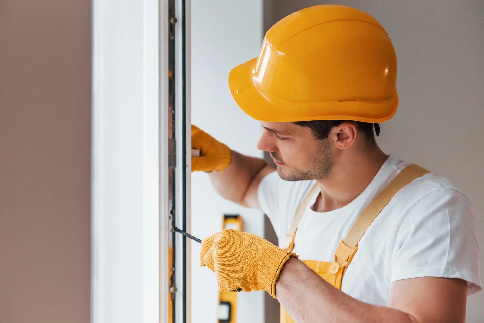 A professional handyman in a hard hat and work gloves adjusting a window frame seal, the kind of precise fit Phoenix heat and dust demand.