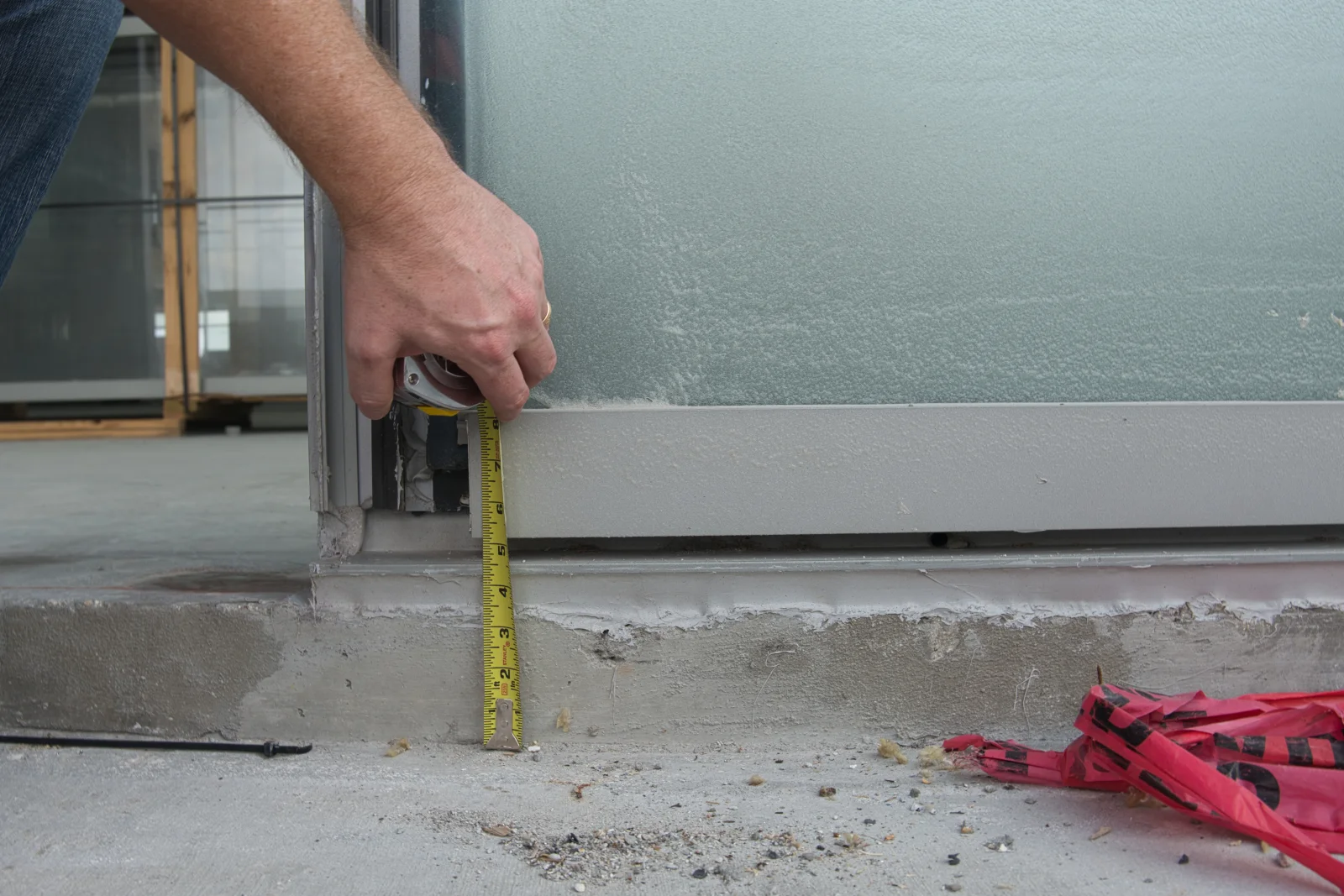 A technician measuring the gap at the base of a sliding glass door to diagnose where weather stripping has failed and dust is getting in.