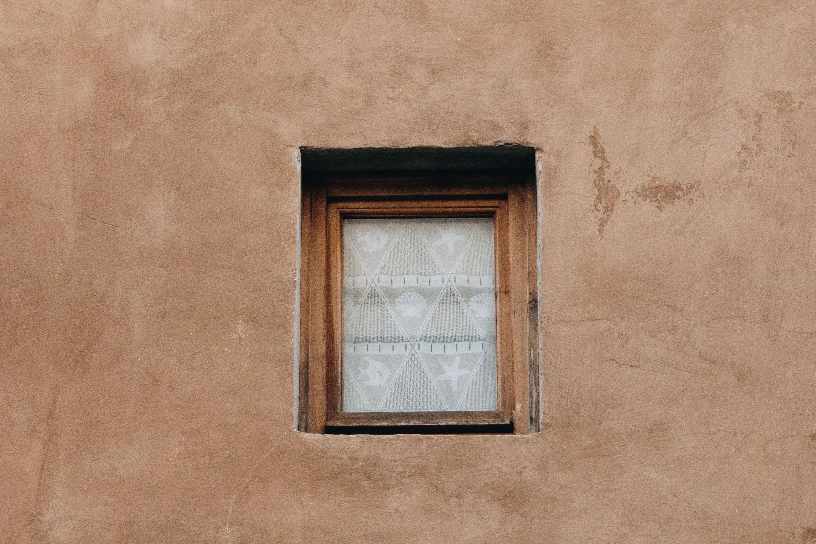 window-repair-phoenix-desert-conditions A weathered wood window frame set into a sun-baked adobe stucco wall on a Phoenix desert home, showing the kind of prolonged UV exposure that dries out seals and warps frames.