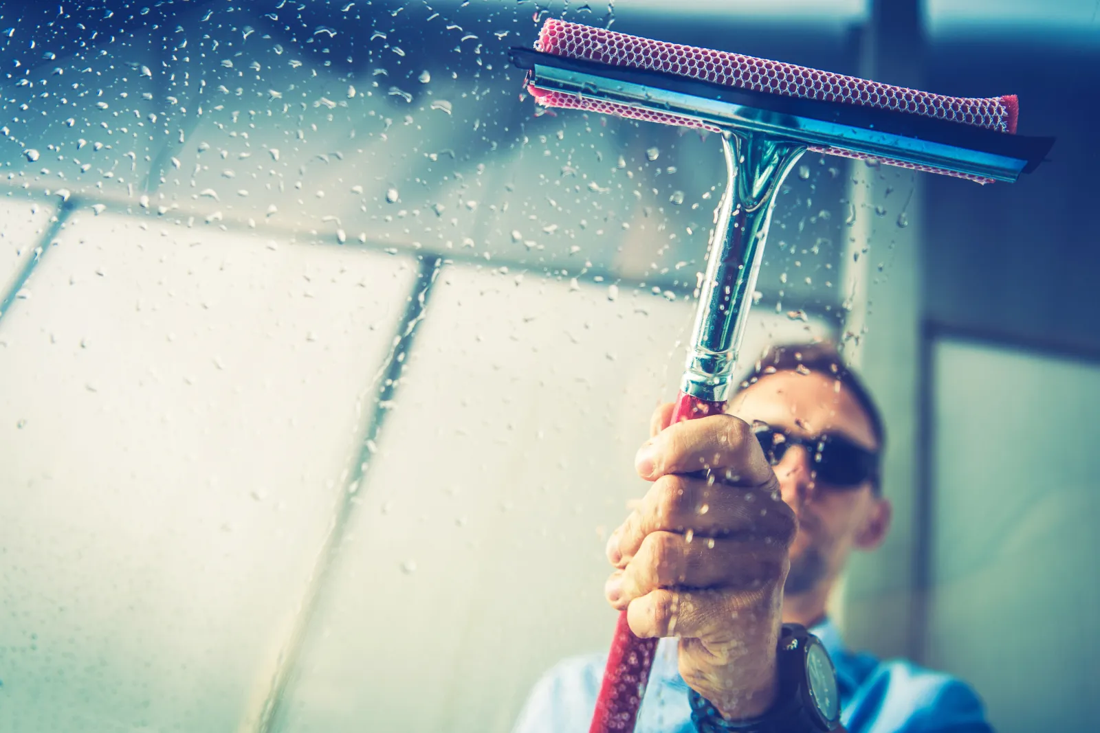 window-washing-phoenix-hard-water-spots A professional window washer using a squeegee to clear hard-water spots and desert dust from sunlit glass on a Phoenix home.