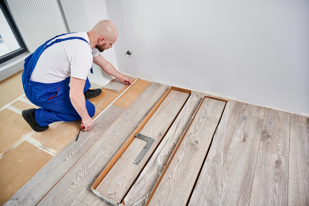 wood-floor-installation-phoenix-contractor-measuring-planks Wood floor installation in Phoenix, Arizona — a contractor in coveralls measuring and fitting engineered wood planks.