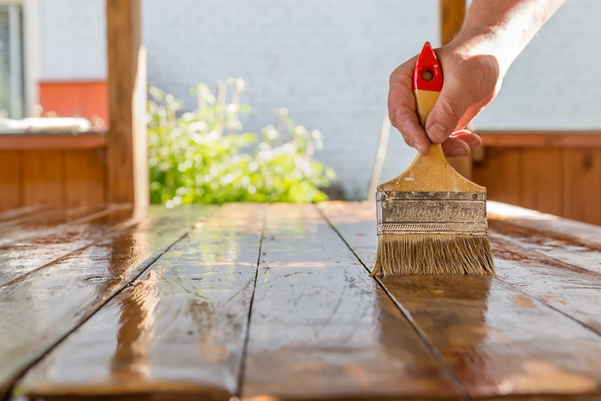 wood-staining-phoenix-hero Wood staining in Phoenix - a paintbrush applying rich stain to sun-bleached deck boards.