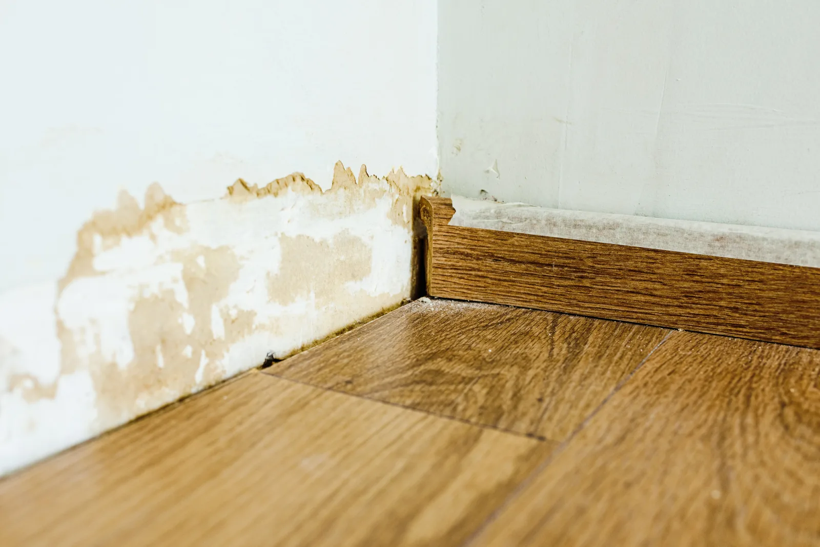wood-trim-phoenix-cracked-baseboard A close-up of cracked, gapped wood baseboard trim pulling away from the wall in a Phoenix home, showing the joint damage caused by desert heat and dry air.