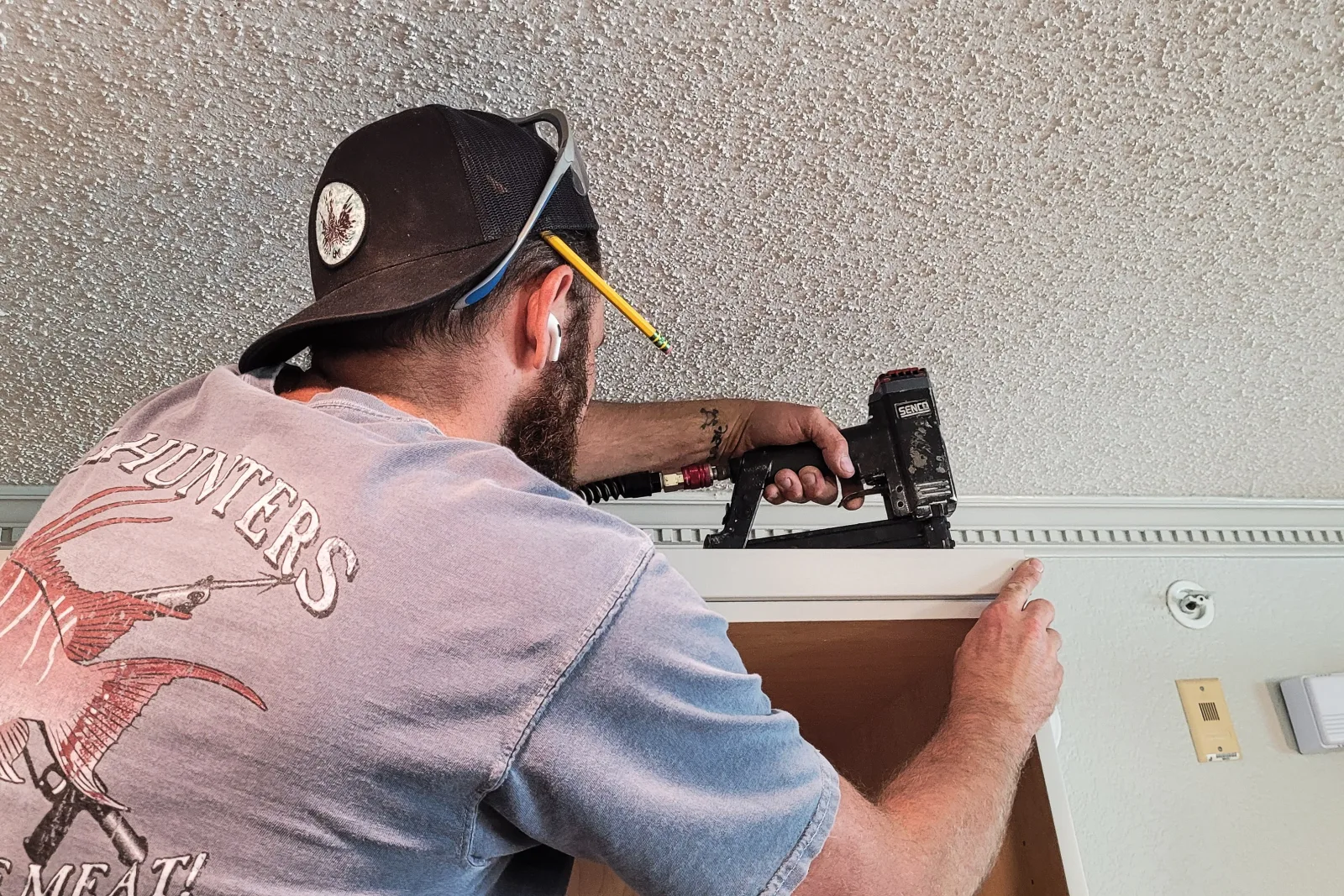 wood-trim-phoenix-crown-molding-install A carpenter uses a pneumatic nail gun to install crown molding along the top of a cabinet against a textured ceiling in a Phoenix home.